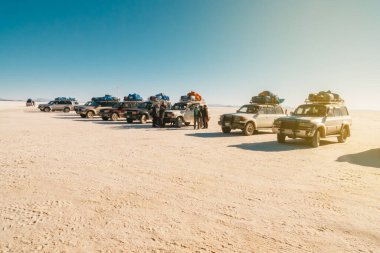 Salar de Uyuni 'de gün batımı ışınları olan bir dinlenme alanına park edilmiş arazi araçları.