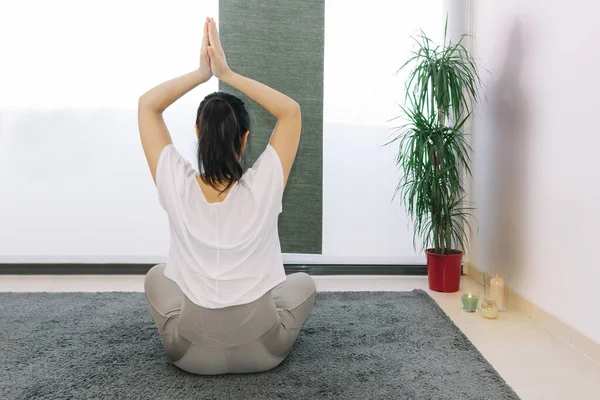 Yoga pozisyonunda oturan kadın mumların ve bitkilerin yanında, evinde dinleniyor.