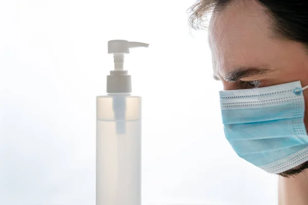 Dezenfektan jel kutusunun önünde arka ışıklandırmalı mavi maske takan adam.