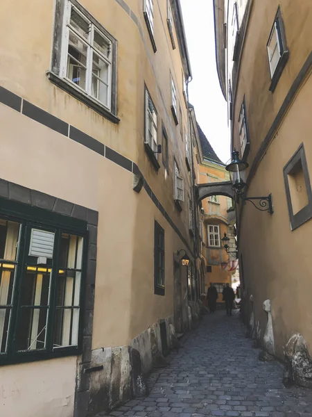 Cityscape of small street between old houses in Vienna city. Historic part of touristic way in urban city. Yellow facade with green windows, between 2 houses small bridge. Touristic concept.