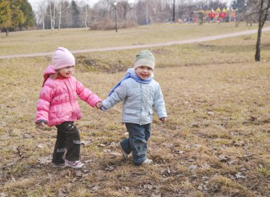 Oğlan ve kız birbirlerini tutuyorlar ve parkta insanlar olmadan yürüyorlar. İkizler için mavi ve pembe renkler. Bahar mevsiminde kardeşlerin aile fotoğrafı..