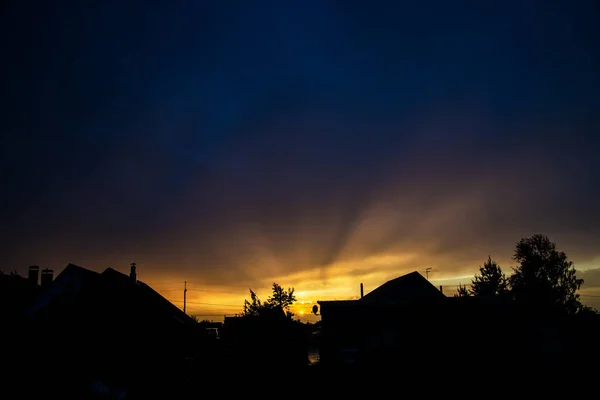 Sunset in the village with bright sunshine and blue sky. Silhouette of small houses with bright flaming shade of sun. Adorable view with copy space. Breathtaking view when night coming.