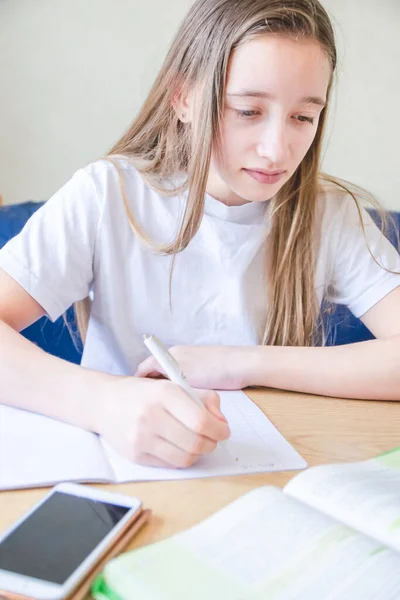 Porträtt av flicka i vit t-shirt sitter och gör läxor — Stockfoto