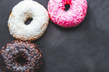 Sol tarafta beyaz, pembe ve çikolata renkli çörekler var.