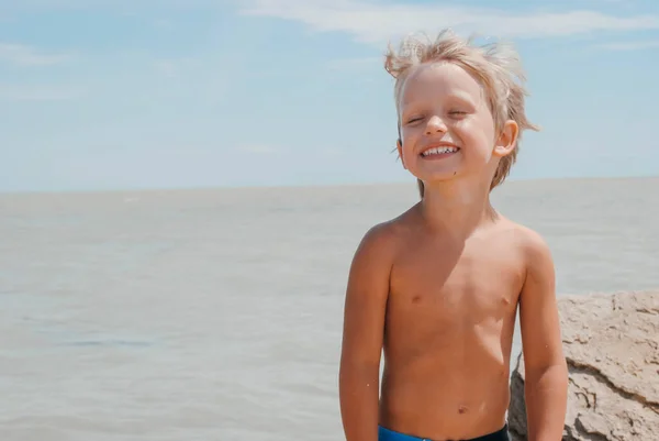 Αγόρι που στέκεται στην παραλία την ηλιόλουστη μέρα και γελάει Royalty Free Φωτογραφίες Αρχείου