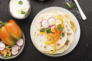 Geleneksel ev yapımı düz ekmek taze mevsim sebzeleri, otlar ve zeytinyağı ve arka planda gül tuz yoğurt sos ile bir şeyler atıştırmak için. Üstten görünüm.