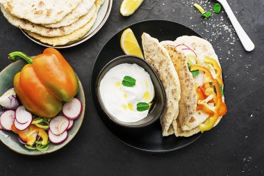 Geleneksel ev yapımı düz ekmek taze mevsim sebzeleri, otlar ve zeytinyağı ve arka planda gül tuz yoğurt sos ile bir şeyler atıştırmak için. Üstten görünüm.