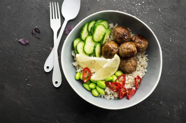 Baked teriyaki meat balls with brown rice, cucumbers, hot pepper, lemon slices in a bowl. Top View clipart