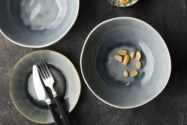 Gray serving plates on a dark gray background for serving lunch. A few peanuts nuts in the frame. Top view