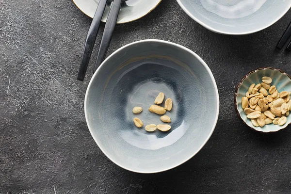 Gray serving plates on a dark gray background for serving lunch. A few peanuts nuts in the frame. Top view