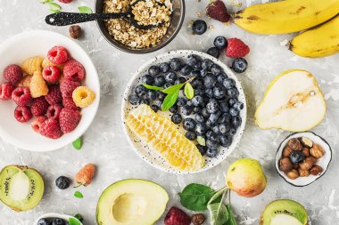 Sağlıklı kahvaltı malzemeler: granola, Mısır gevreği, fındık, çilek, meyve, avokado, ahududu, yaban mersini, bal tarak, armut elma kivi muz lif ve vitamin en iyi görünümünü tam