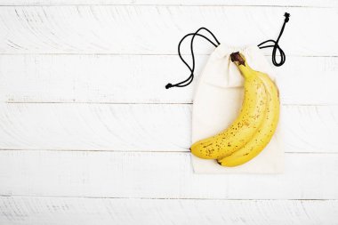 Beyaz ahşap zemin üzerinde beyaz pamuklu Eko çanta üzerinde muz. Alışveriş yok plastik sıfır atık ev kavramı. Uzay kopyalayın. Üstten görünüm