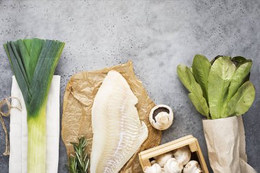 Alışveriş sıfır atık ürünler. Morina fileto, petrol, pırasa, marul alımları için bir zanaat kağıt torba ile hafif bir arka plan üzerinde. Üstten görünüm. Gri arka planı.