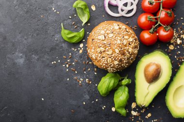 Avokado ile hamburger maddeler. Sebze burger kepekli çörek, avokado, tatlı soğan, domates, fesleğen karanlık bir arka plan üzerinde yapılır. Üstten görünüm, uzay.