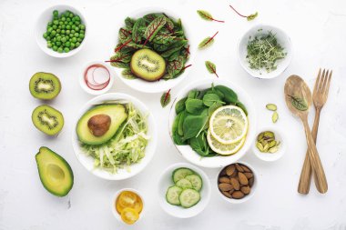 Bahar için yeşil malzemeler detoks salata: ıspanak, Kırmızı damarlar, salatalık, turp, marul, yeşil bezelye, avokado, limon, microgreen, beyaz bir zemin üzerine sarı domates ile kuzukulağı