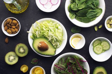 Yemek taze yeşil salata. Buzdağı bırakır, ıspanak, kuzukulağı, salatalık, turp, avokado, sağlıklı bir diyet için limon. Karanlık bir arka plan üzerinde. Üstten görünüm.