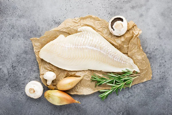 Wild northern white cod fillet fillet on parchment with shallot onions, olive oil, thyme, rosemary, champignons for cooking healthy meals for the whole family. Top view.