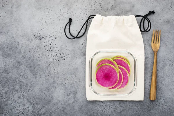Watermelon radish slices in a snack container on a cotton eco bag with wooden cutlery. Healthy food zero waste house. Sveeru view.