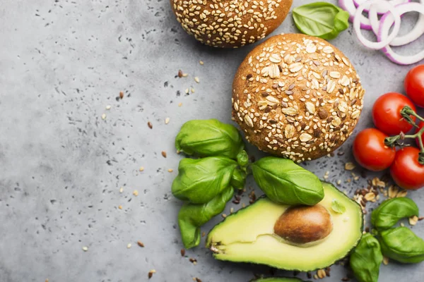 Healthy food. Veggie burger ingredients cereal buns, avocado, cherry tomatoes, basil, sweet onions on a light gray background. Top view, space. — Stock Photo, Image