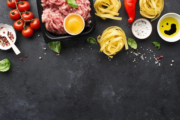 Minced meat, egg, pasta, basil, salt, pepper, ingredients for home cooking. On a dark background. Top view