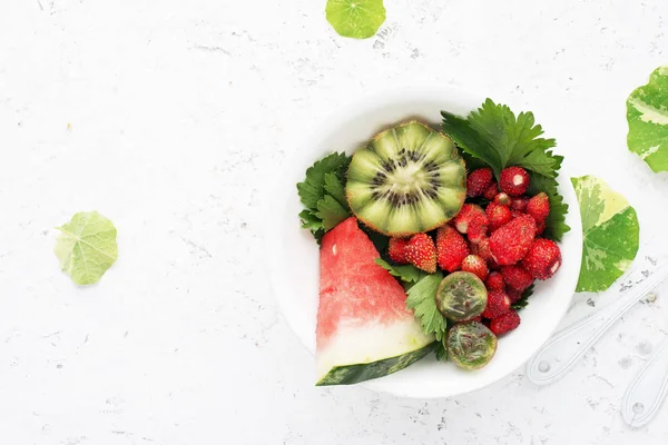 Fruit salad. Watermelons, strawberries, kiwi, nasturtium leaves for pure nutrition. On a light background. Top view.