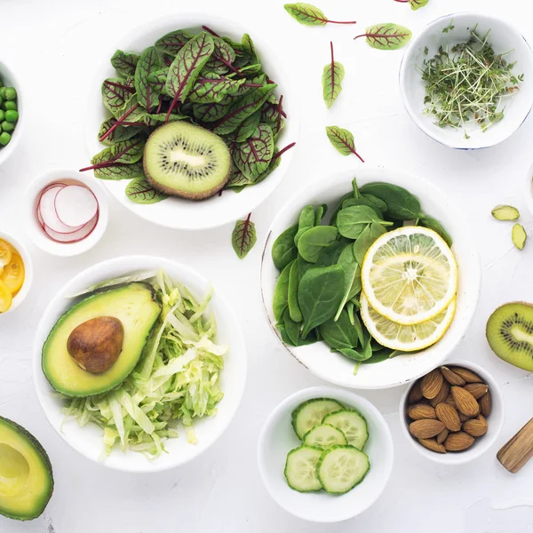 Zelené ingredience pro jarní detox saláty: špenát, šťovík, červené žilky, okurky, ředkvičky, salát ledový, zelený hrášek, avokádo, citron, microgreen, žlutá rajčata na bílém pozadí s — Stock fotografie