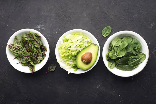 Cuisson de salade verte fraîche. Feuilles d'iceberg, épinards, oseille, concombres, radis, avocats, citron pour une alimentation saine. Sur un fond sombre. Vue du dessus . — Photo