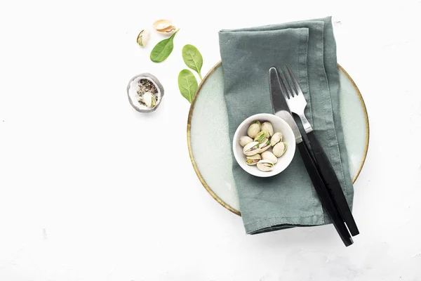 Plaat op tafel met bestek en linnen servet in olijf onah met pistachenoten. Bovenaanzicht. — Stockfoto