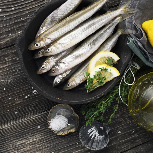 Utile petit poisson de mer. Éperlan, sardine, anchois avant cuisson au sel, citron, beurre, thym sur fond de bois. Vue du dessus . — Photo