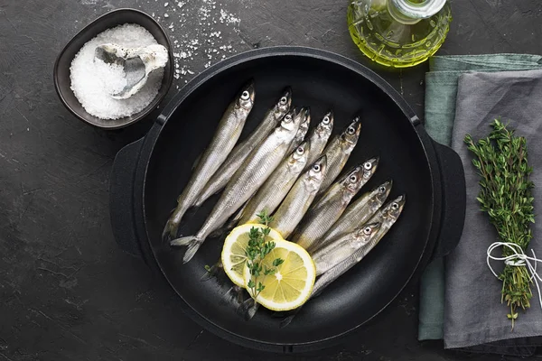 Petit poisson de mer éperlan ou sardine avant cuisson en fonte pour la cuisson au citron, au beurre et au sel. Vue de dessus. Sur un fond sombre . — Photo