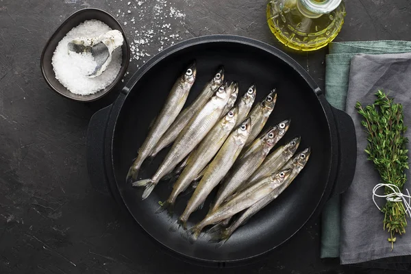 Los pequeños peces de mar olían o sardina antes de cocinar en forma de hierro fundido para hornear con limón, mantequilla y sal. Vista superior. Sobre un fondo oscuro . — Foto de Stock