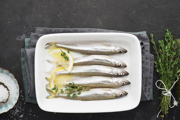 Fresh sea cold-water small fish such as smelt, sardine, anchovies on a simple background with lemon slices, for the concept of correct healthy natural nutrition. Top View.