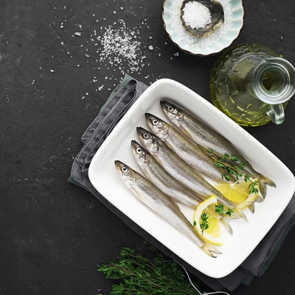 Fresh sea cold-water small fish such as smelt, sardine, anchovies on a simple background with lemon slices, for the concept of correct healthy natural nutrition. Top View.