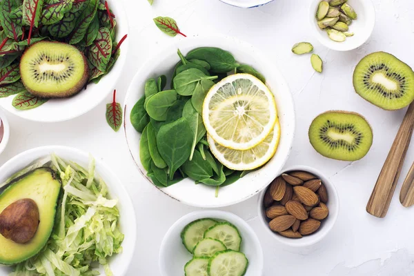 Zelené ingredience pro jarní detox saláty: špenát, šťovík, červené žilky, okurky, ředkvičky, salát ledový, zelený hrášek, avokádo, citron, microgreen, žlutá rajčata na bílém pozadí s Stock Snímky