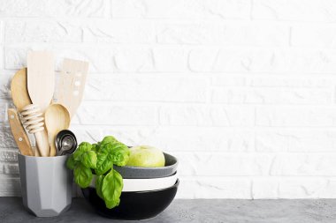 Mutfak araçları, zeytin kesme tahtası beyaz duvara karşı bir mutfak raf. Seçici odak. Taze fesleğen ve limon. Siyah ve beyaz modern çatal bıçak takımı. Plastik ev