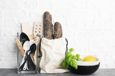 Mutfak araçları, zeytin kesme tahtası beyaz duvara karşı bir mutfak raf. Seçici odak. Taze fesleğen ve limon. Siyah ve beyaz modern çatal bıçak takımı. Plastik ev