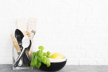 Mutfak araçları, zeytin kesme tahtası beyaz duvara karşı bir mutfak raf. Seçici odak. Taze fesleğen ve limon. Siyah ve beyaz modern çatal bıçak takımı. Plastik ev
