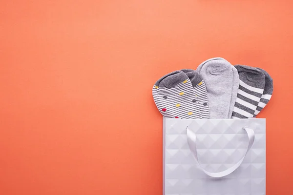 Nuevos calcetines grises diferentes en una bolsa de papel textural gris sobre un fondo de color pastel .. Imagen De Stock