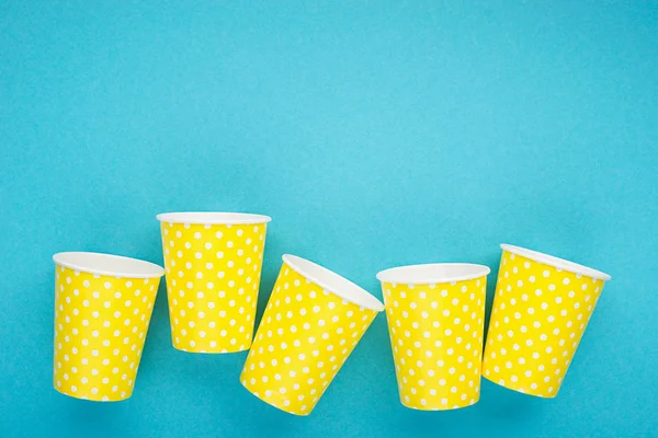 Paper yellow cups on a blue background. The main concept of plastic free on a clean planet. Horizontal, copy space