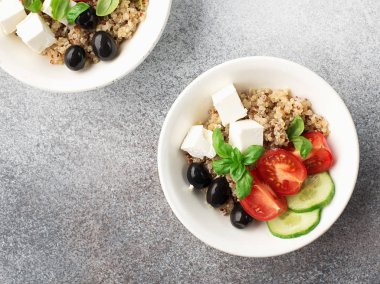 Quinoa, salatalık, domates, beyaz bir tabakta gri bir arka plan üzerinde fesleğen yaprakları ile sağlıklı dengeli iştah açıcı salata kase