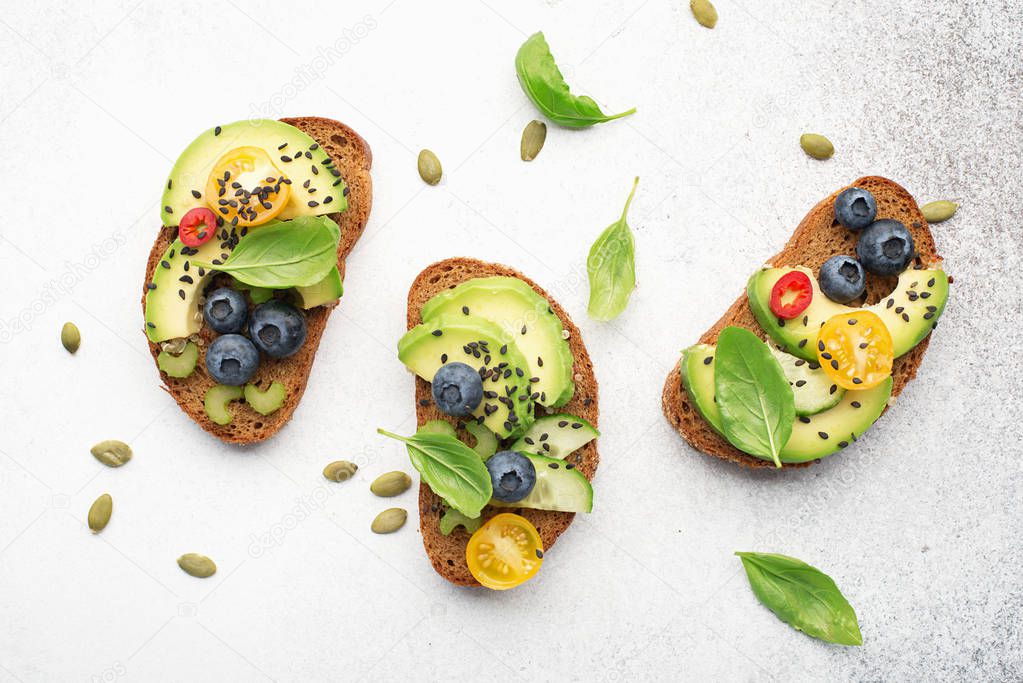 Healthy balanced nutrition. Open sandwiches on whole wheat dark bread with avocado, celery, blueberries, cherry tomatoes. Bright juicy finger snacks. Top view. On a light background,