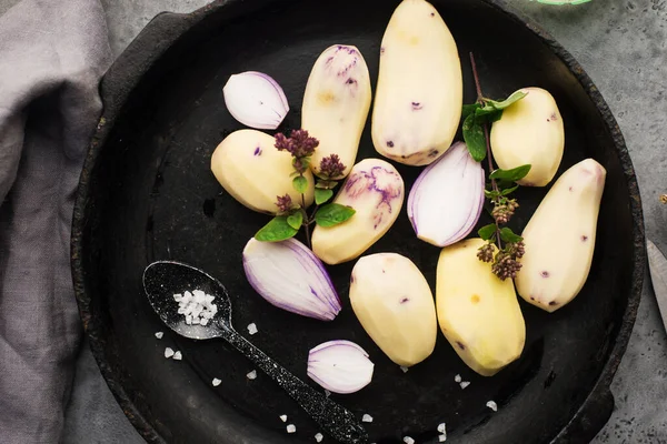 Sliced purple young raw potatoes before baking in a pan with onions, butter, and oregano. Top view. Comfortable homemade food. Flat lay, — Stock Photo, Image