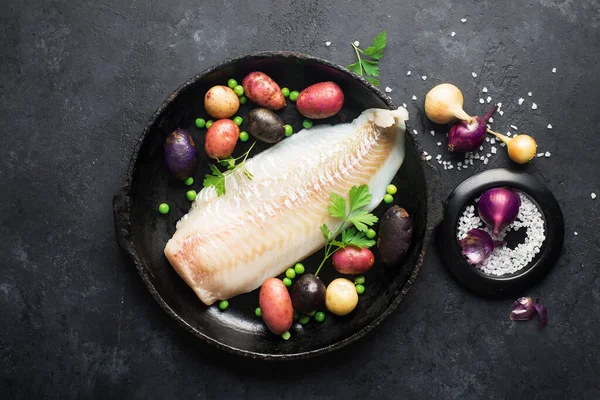 Bacalao pescado blanco patatas plato ingredientes para una comida casera cómoda y saludable. Filete de pescado blanco crudo en una bandeja para hornear sobre un fondo oscuro. Vista superior., Fotos De Stock