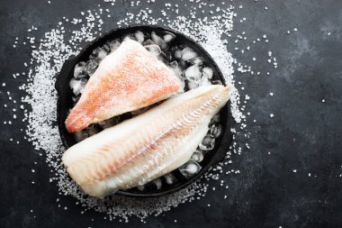 Beyaz deniz soğumuş balık filetosu buz küpleri içinde koyu bir arka planda. Üst görünüm.