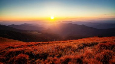 Dağ tepeleri ve tepeler üzerinde renkli otlarla dolu güzel, canlı bir günbatımı.