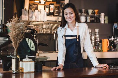 Asyalı kadın barista aşınma jean önlük sayaç çubuğunda elini yerleştirin ve müşteriye, Cafe hizmet anlayışı, gülümseyen sahibi iş başlamak yukarıya.