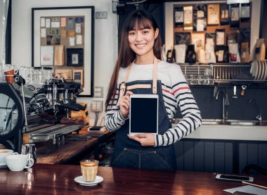 Asyalı kadın barista aşınma jean önlük gülümseme duygu, Cafe restoran hizmet kavramı, yukarıya aygıt ekran metni küçük business.mock sahibi olan sayaç bar müşteri için boş ekran tablet holding