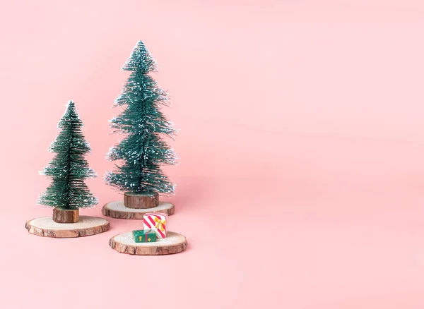 Tree Christmas tree on wood log slice with present box on pastel pink studio background.Holiday festive celebration greeting card with copy space for display of design or content