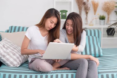 İki Asyalı kadın evde oturma odasında kanepede oturuyor ve online alışveriş için dizüstü bilgisayar kullanarak. Dijital yaşam tarzı. Lezbiyen lgbt çift