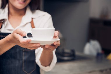 Asya kadın barista aşınma jean önlük sıcak kahve fincanı bar sayacı, yüze gülen ile müşteriye hizmet tutan Cafe restoran hizmet concept.waitress çalışma